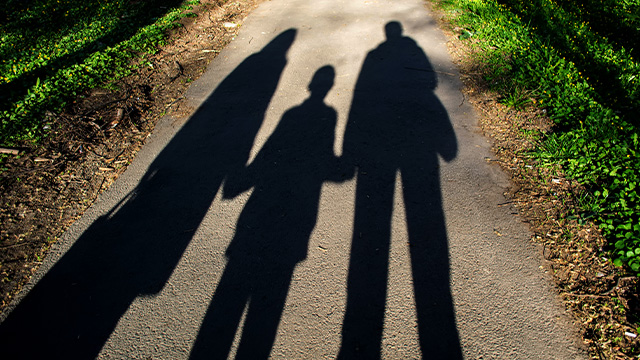 shadows of parents and child across paved road